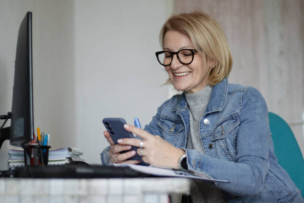 istock Mature blonde woman with glasses working online on computer and using mobile phone 2194511714