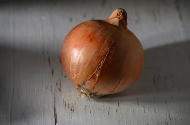 A brown onion sits on a weathered wooden surface, its surface reflecting soft natural light, highlighting its cracks.