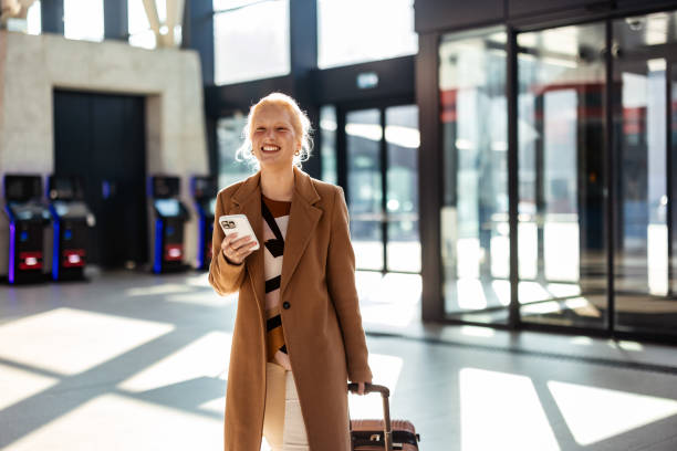 istock Businesswoman walking through airport terminal pulling suitcase and using smartphone 2194513096