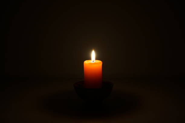 A single orange candle burns brightly in the darkness, casting a warm glow and creating a peaceful and contemplative atmosphere.