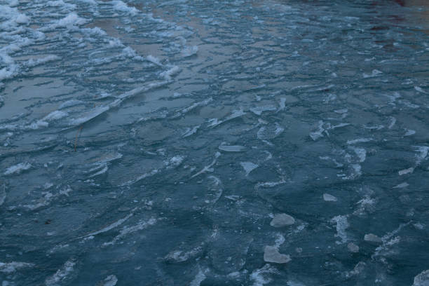A close-up view of a frozen lake surface reveals intricate ice patterns and textures. The frosty details shimmer under the soft winter light, creating a captivating natural design.