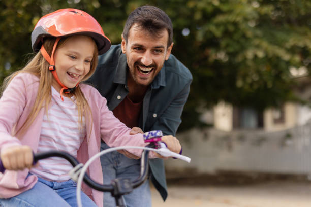 istock Smiling Father Supporting His Daughter While Learning to Ride a Bike 2194522345