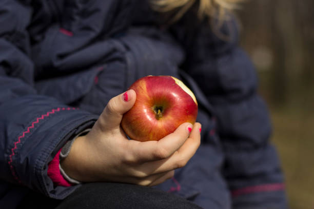 Child holds a bright apple while sitting outdoors