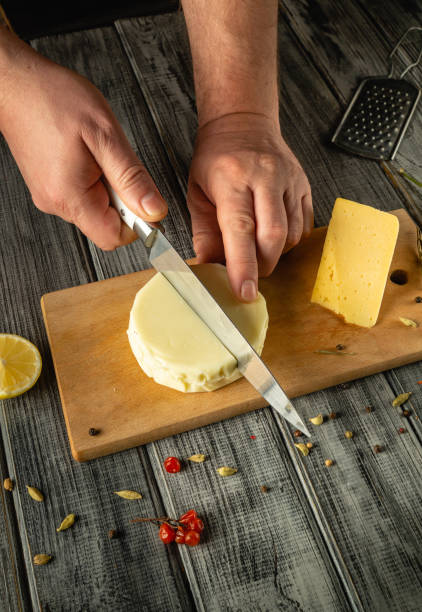 istock Skilled hands slice a round cheese on a wooden board with fresh lemon and spices scattered around. The warm kitchen exudes a cozy atmosphere, perfect for culinary creation 2194525937