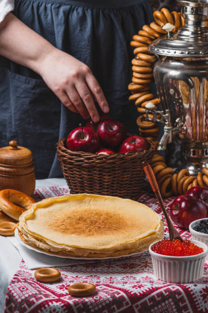 istock Pancakes on the table with traditional patterns, next to the samovar and caviar. From behind, a woman's hand takes an apple from a basket 2194529163