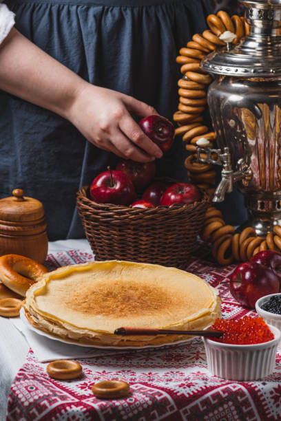 istock Pancakes on the table with traditional patterns, next to the samovar and caviar. From behind, a woman's hand takes an apple from a basket 2194529167