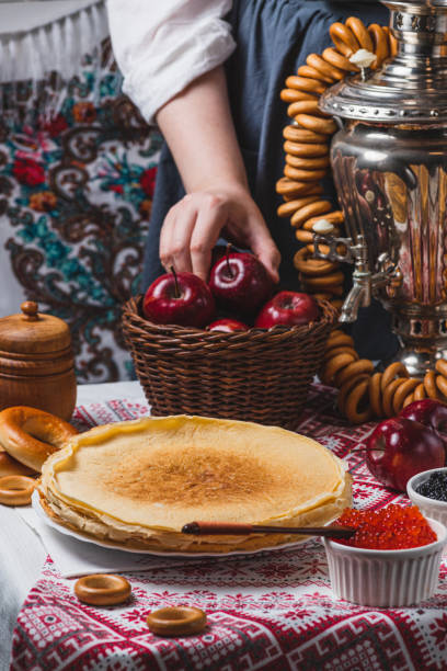 istock Pancakes on the table with traditional patterns, next to the samovar and caviar. From behind, a woman's hand takes an apple from a basket 2194529176