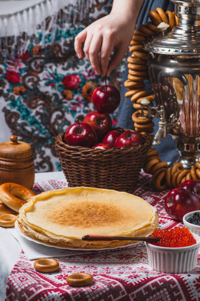istock Pancakes on the table with traditional patterns, next to the samovar and caviar. From behind, a woman's hand takes an apple from a basket 2194529178