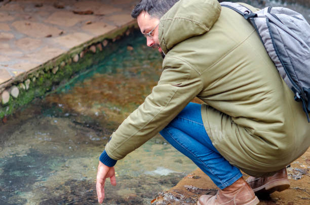 istock A man crouches to touch the warm water flowing through a man-made channel 2194529787