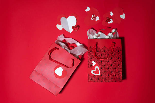 Front view of two paper shopping bags at the left of the image leaving a useful copy space at the right side on a pink background. Eachbags has a heart shaped paper.