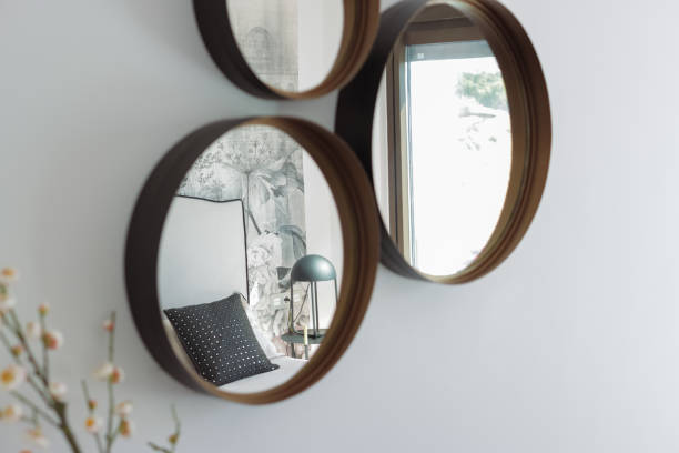 istock Three round mirrors with wooden frames are hanging on a white wall, reflecting a modern bedroom interior with floral wallpaper, a comfortable bed, and a stylish lamp 2194537083