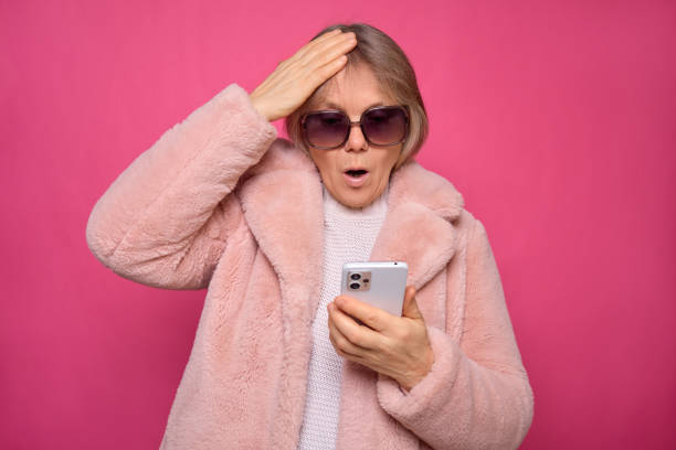 istock A surprised woman wearing oversized sunglasses is checking her smartphone with a shocked expression. She is dressed in a fluffy pink coat and is indoors against a vibrant pink backdrop 2194539721