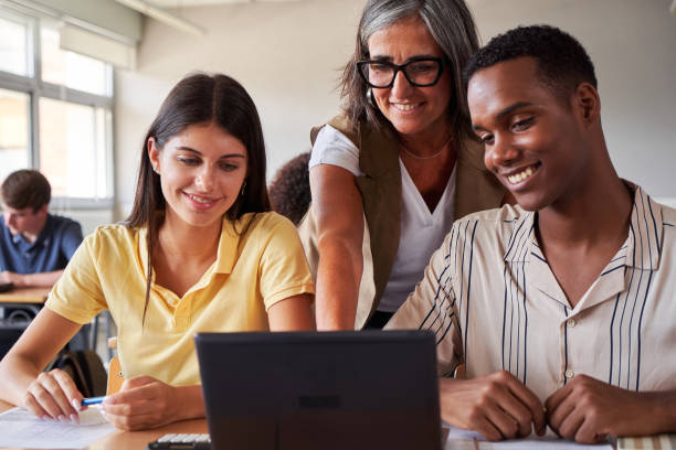 istock Smiling female teacher helping two multiracial college students using laptop to study in classroom. 2194541666