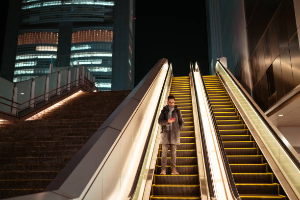 Man going down the escalator on the street is using a phone.