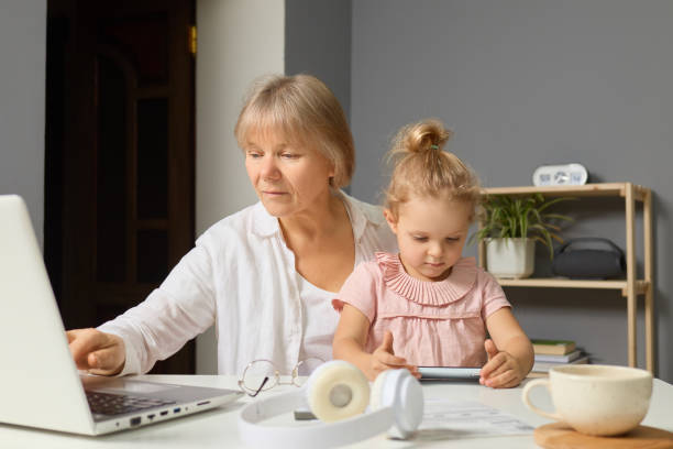 istock A grandmother helps her young granddaughter with an online learning activity while sitting at a table in a cozy home environment during the afternoon 2194545728