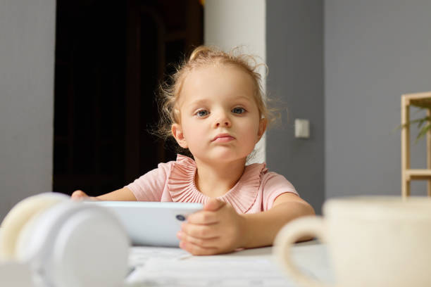 istock A young girl sits at a table with a tablet in her hands, displaying concentration. Sunlight fills the room, creating a warm and inviting atmosphere 2194545756