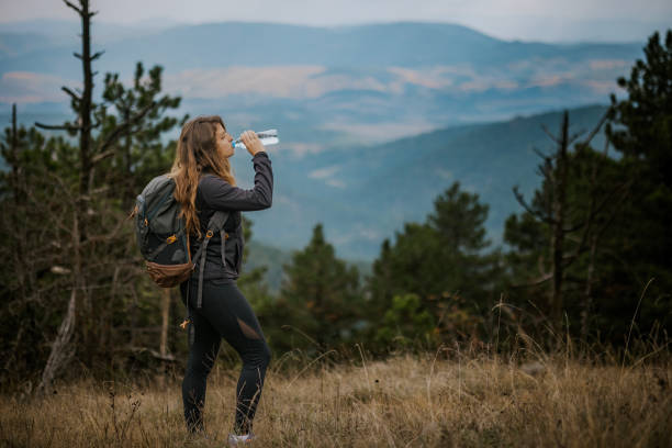 istock A hiker pauses to drink water while exploring scenic mountains on a cool day, surrounded by lush forest and rolling hills in the background 2194554590