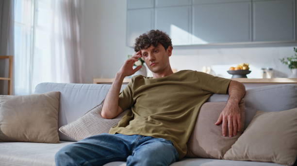 istock Sad guy thinking problems in modern living room apartment. Brunet watching tv 2194557844