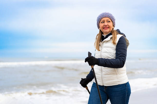 Mature woman exercising Nordic walking on beach. Winter