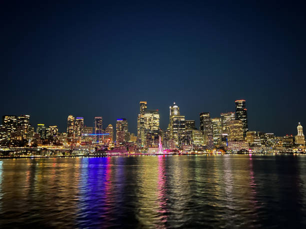 Seattles skyline at night with a glowing Ferris wheel, skyscrapers, and reflective waters on the Puget Sound.
