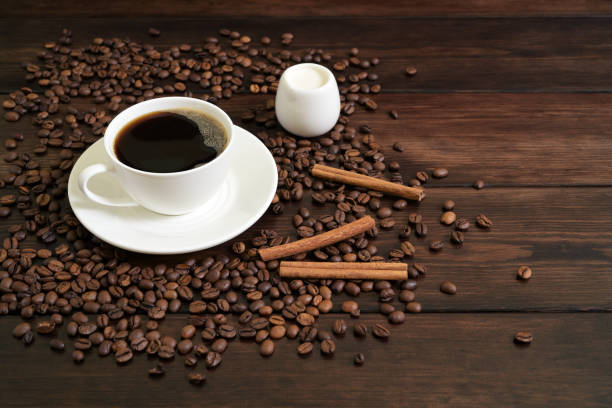 istock White Coffee Cup with Black Coffee, Creamer, Cinnamon Sticks, and Coffee Beans on Wooden Surface 2194564370