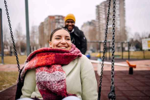 Young adults having fun in public park swinging each other
