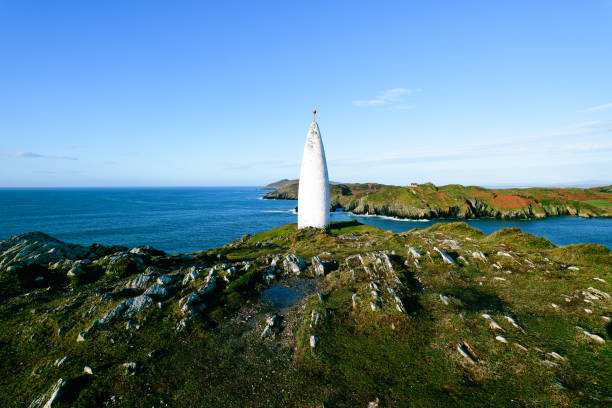 istock Seascape with structure. A tall, white, pointed tower is situated on a grassy, rocky headland. The ocean stretches to the horizon under a bright blue sky. 2194575493