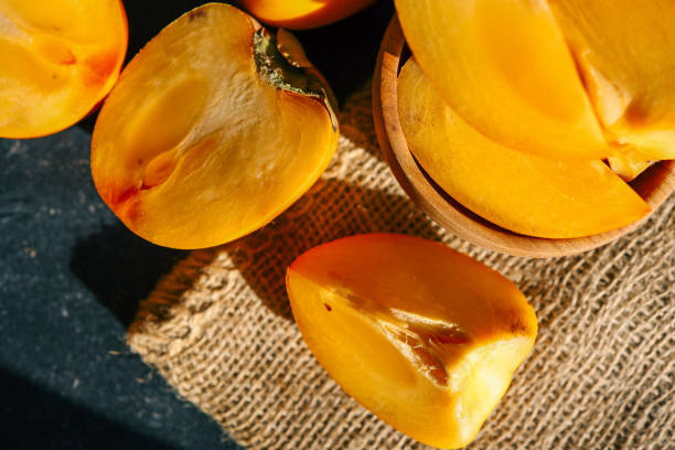 istock Sliced and whole persimmons arranged on a dark textured surface with natural light and burlap, showcasing vibrant colors and rustic simplicity. Perfect for food, seasonal, and healthy living themes 2194576950