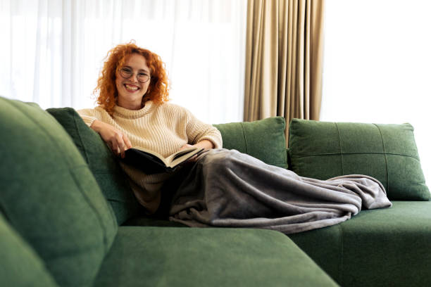 istock Beautiful Young woman sitting on a sofa and reading a book 2194578529
