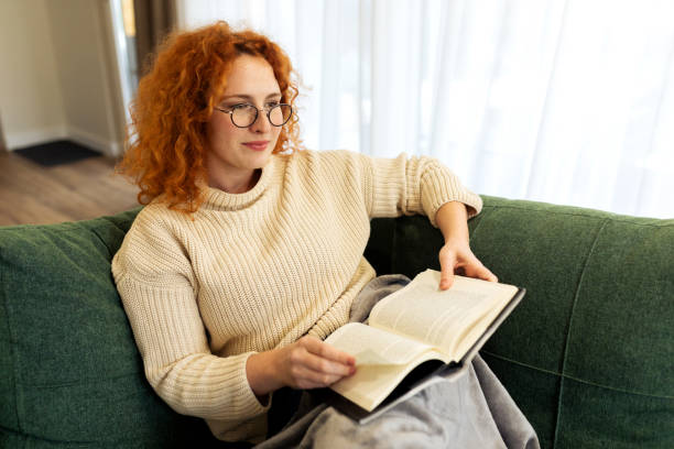 istock Beautiful Young woman sitting on a sofa and reading a book 2194578603