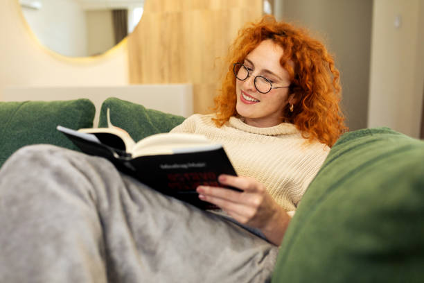 istock Beautiful Young woman sitting on a sofa and reading a book 2194578657