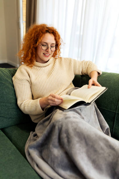 istock Beautiful Young woman sitting on a sofa and reading a book 2194578660