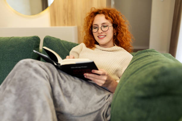 istock Beautiful Young woman sitting on a sofa and reading a book 2194578675