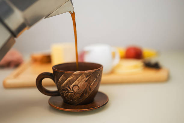 istock Pouring freshly brewed coffee from a moka pot into a brown clay cup and preparing breakfast on a table in the kitchen 2194584155