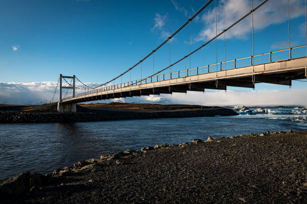 istock Suspension bridge spans a river with dramatic clouds in the background against a serene landscape 2194590241
