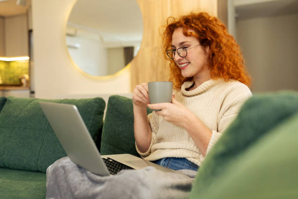 istock Young woman sitting on the sofa in her living room while using laptop computer and drinking coffee 2194590575