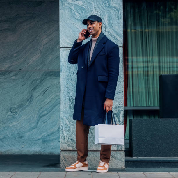 istock Stylish Man Talking on Mobile Phone While Standing Outdoors Holding a Shopping Bag 2194591251