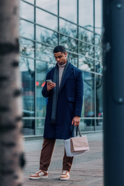 istock Stylish Man Holding Shopping Bags While Using Smartphone Outdoors 2194591254