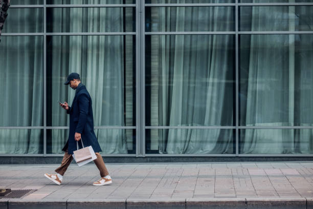 istock Man Walking Downtown While Using Smartphone and Holding Shopping Bag 2194591257