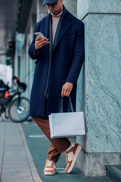 istock Stylishly Dressed Man Using Smartphone Outdoors Holding Shopping Bag 2194591265