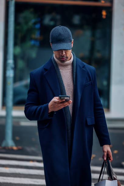 istock Man in Stylish Coat Walking While Using Smartphone in Urban Street 2194591291