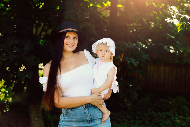 A beautiful mom holding her 16 month old daughter outside. Her daughter is wearing an outfit that she wore when she was a baby.