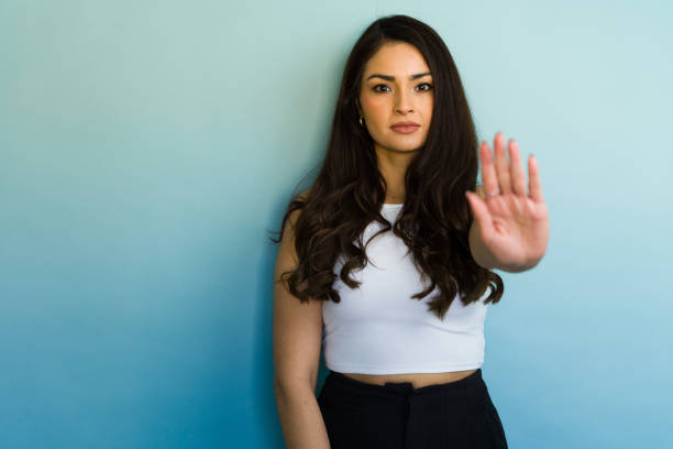 Confident and serious young woman gesturing to stop against a blue background, expressing a clear message of refusal or boundary setting
