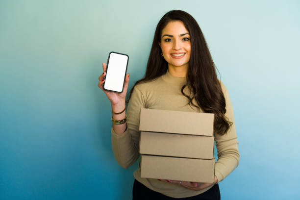 istock Online seller holding cardboard boxes and showing smartphone with blank screen 2194592263