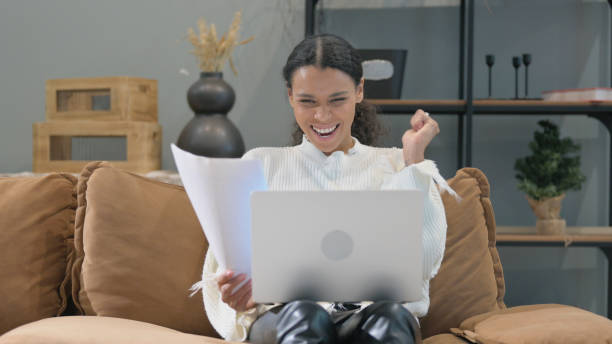 istock Cheering African Woman celebrating Paperwork with Laptop 2194597661