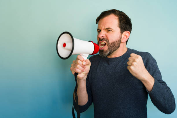 istock Angry man shouting with megaphone on blue background 2194598161