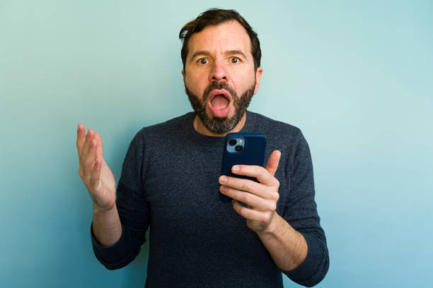 istock Surprised man reading news on mobile phone on blue background 2194598927