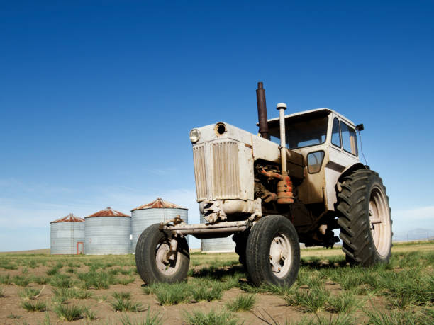 Old tractor in the field next to some silos, blue sky and copy space