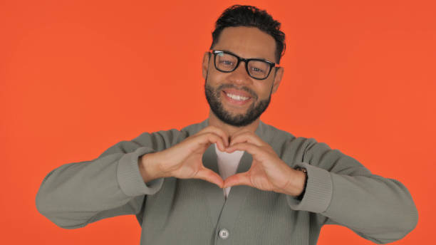istock Casual Hispanic Man with Heart Sign with Hands on Red Background 2194604170
