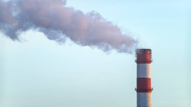 istock A factory chimney with red stripes smokes against a blue sky. 2194605423